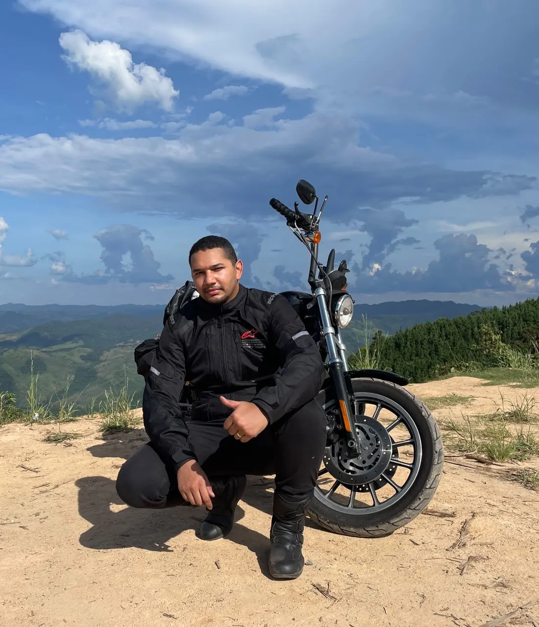 André Miranda ao lado da moto no alto de uma serra